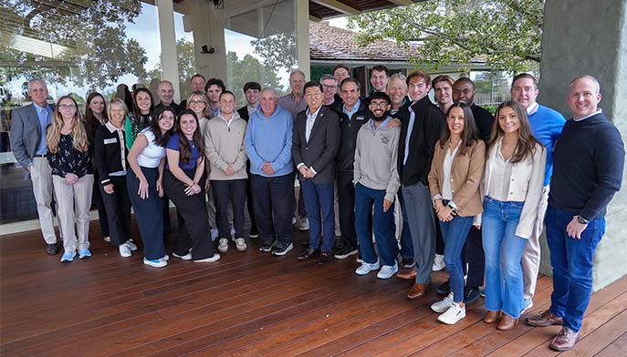Image of a group of Dolan students, faculty, and alumni standing together on a wooden deck
