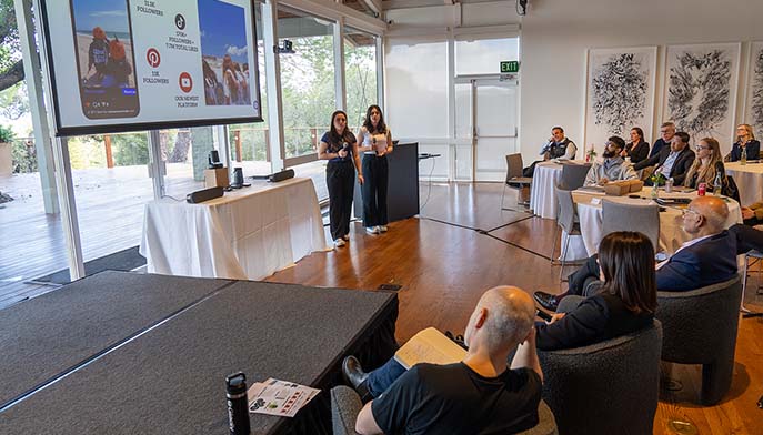 Image of a group of people seated in chairs, watching a presentation on a large screen in front of them.