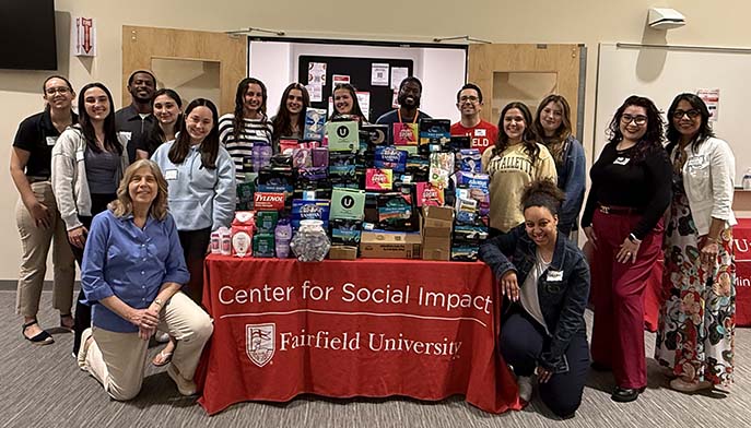 Image of a group of people stands by a table displaying a sign that reads "Centers for Social Impact."