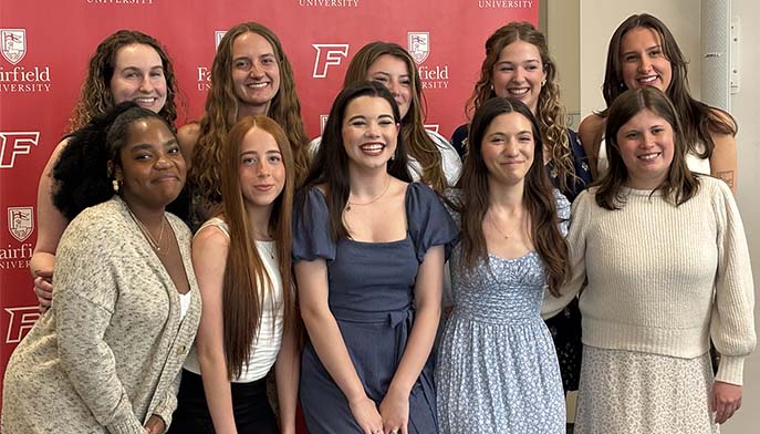 A group of women smiling and posing together in front of a vibrant red wall.