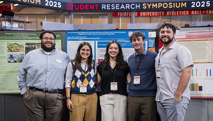 Image of a group of four students stands proudly in front of a poster, showcasing their project.