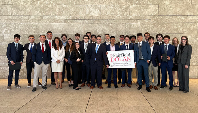 Several students in formal attire, including suits and ties, gather in front of a large office building.  