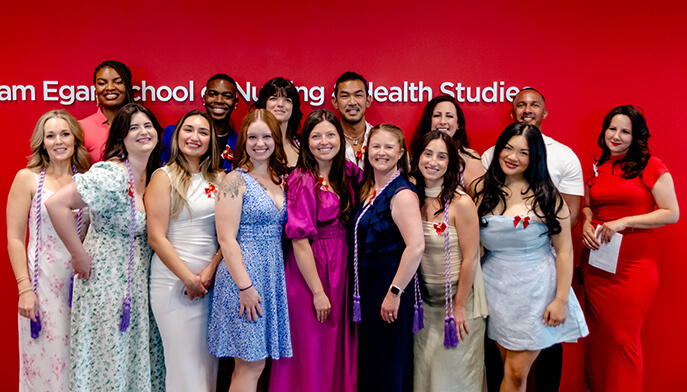 A group of second degree nursing students in colorful dresses and shirts smile and pose together for a photo indoors.. 