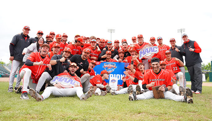 The Fairfield University baseball team stands together on the field, smiling for a group photo in their uniforms.