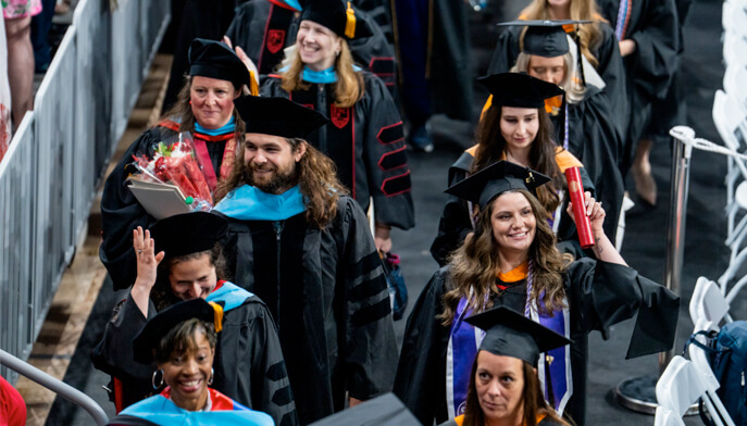 A group of graduates processes down the aisle at commencement, dressed in traditional caps and gowns, filled with pride.