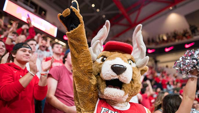 Image of a cheerful Lucas the Stag in red gear pumps up the crowd with excitement and energy.