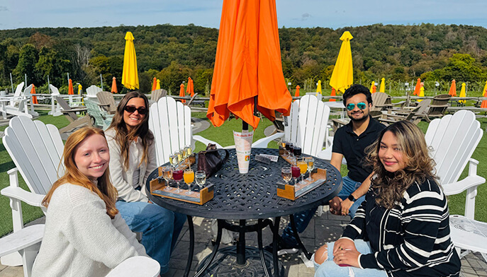 Four people at a table with an umbrella, engaged in conversation in a pleasant outdoor environment.
