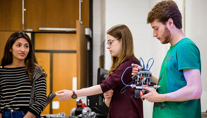 In a lab, students are focused on assembling a robot, using various tools and components for their project.