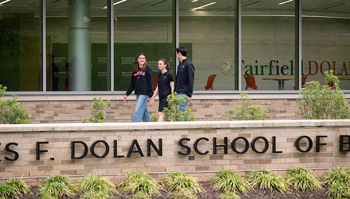 Three individuals stand outside the Charles F. Dolan School of Business, smiling and engaged in conversation.