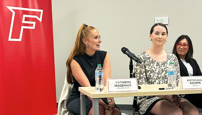Three women seated at a table, each with a microphone, engaged in discussion or presentation.