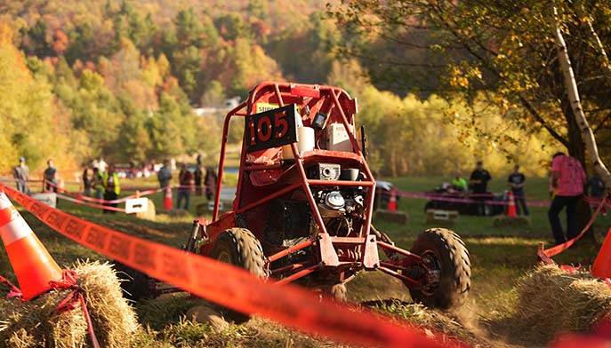 A bright red buggy speeds across a lush field, surrounded by nature.