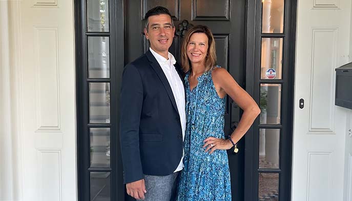 A man and woman stand together in front of a sleek black door, smiling at the camera.