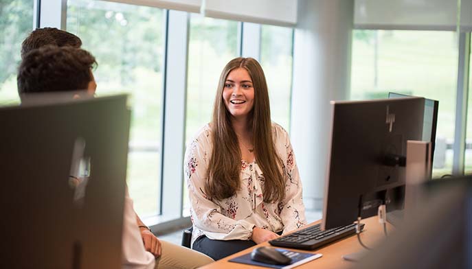 A student focused on their work at a computer in a busy computer lab.