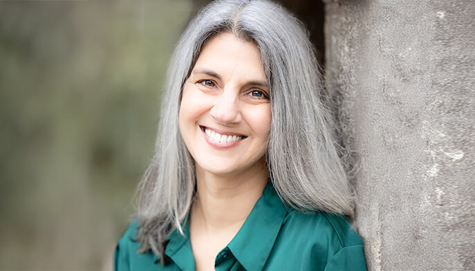 A woman with gray hair wearing a green shirt, smiling softly at the camera.