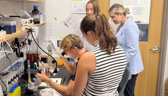 Three women collaborate in a laboratory, focused on a scientific project with various equipment around them.  