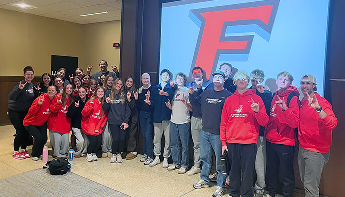 A group of students wearing red shirts stands in front of a large screen featuring the F logo, posing for a photo.