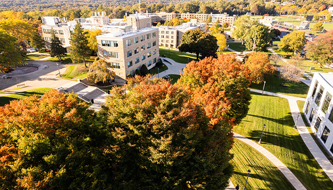 A scenic view of a Fairfield Univesrity campus featuring lush trees and various buildings under a clear blue sky.