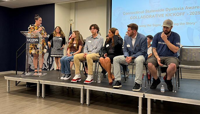 Several individuals on stage, engaged in a discussion while a speaker addresses the audience.