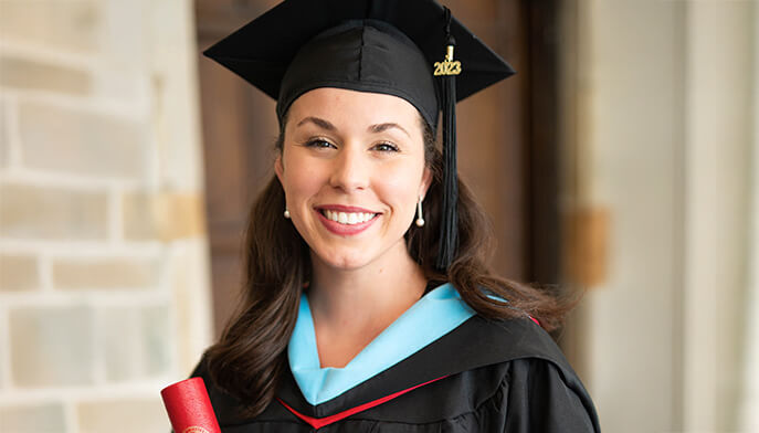 A woman in a graduation gown and cap proudly holds her diploma, celebrating her academic achievement.