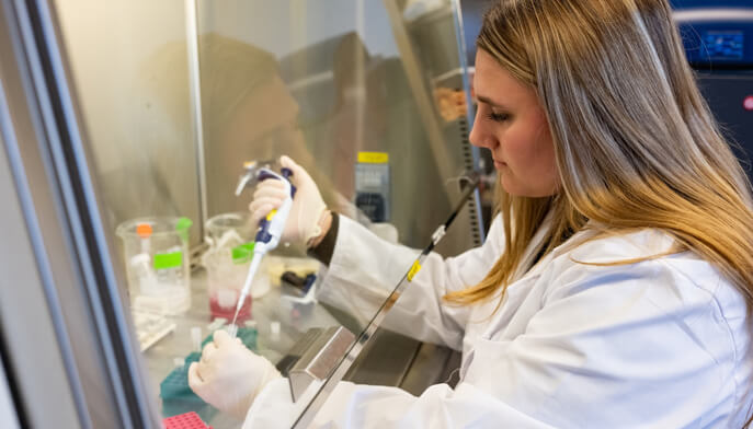 A female student in a lab coat is focused on conducting an experiment at a laboratory workstation.  