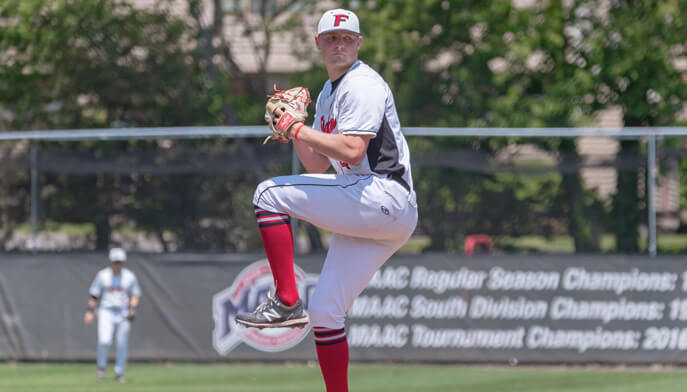 A baseball player in a red and white uniform is in the pitching stance, preparing to throw a baseball.