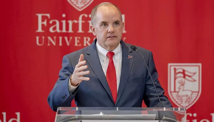 Vice President for Athletics, Paul Schlickmann, giving a speech at a podium in front of a Fairfield-branded banner.