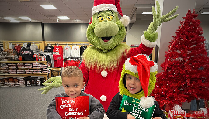 Two smiling children pose in front of a decorated Christmas tree and Grinch, radiating joy and holiday spirit.