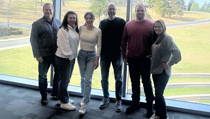 Several people gather in front of big windows, chatting and looking out at the scenery beyond.