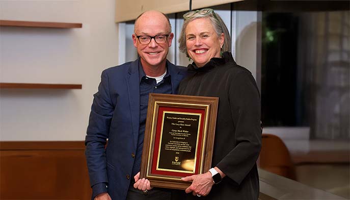 The person on the left is happily accepting an award from the person on the right in a festive setting.