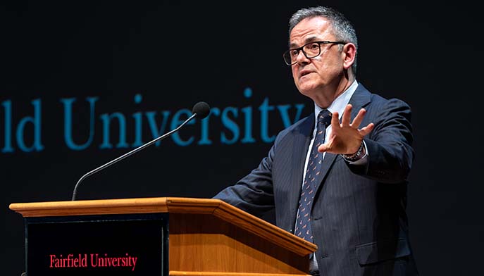 A well-dressed man delivering a speech, standing confidently at a microphone.