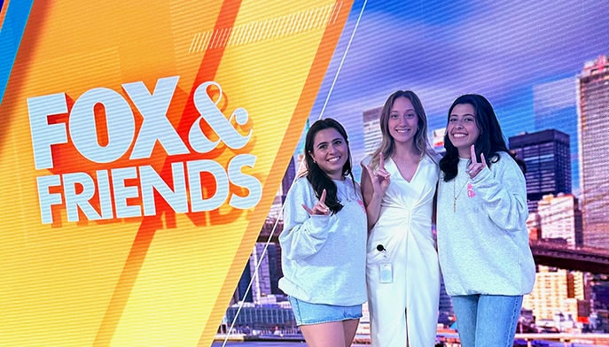 Three Fairfield students posing excitedly in front of the Fox & Friends virtual news background.