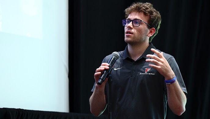 Student-athlete presenting on stage with a microphone for a career in sports forum.