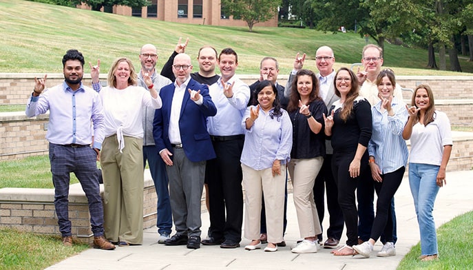The first cohort of Fairfield Dolan's Executive DBA standing and smiling on the Dolan building pathway/lawn in a group.