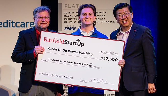 Male business sophomore with two faculty members smiling and holding a prop check for $12,500.