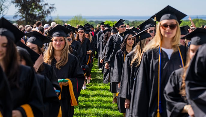 Undergraduate students in caps and gowns processing down Bellarmine Lawn for Fairfield's 75th Commencement ceremony.