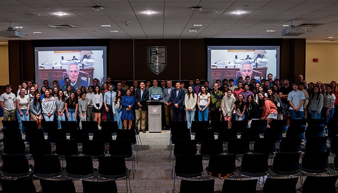 Business students, faculty, and staff posing for a group photo with a Zoom speaker after the launch of the new AI and Tech institute.