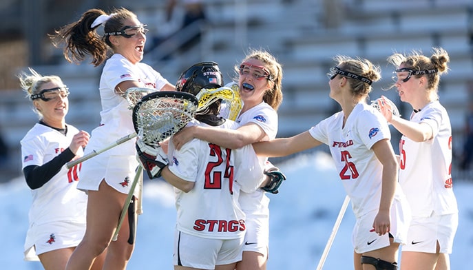 Women's lacrosse players celebrating a victorious game as the final score is announced.