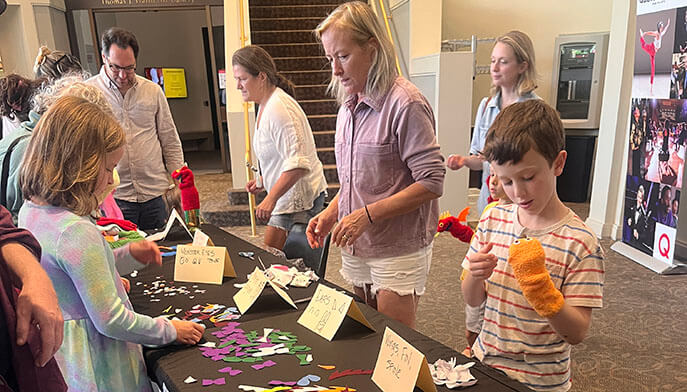 Parents and children creating puppets at a crafts table before a puppetshow performance.