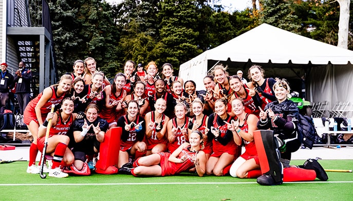 The field hockey team celebrating a win post-game by posing as a group on the field.