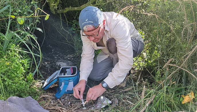 Image of a man kneeling in the grass, fixing a device while collecting samples for research.