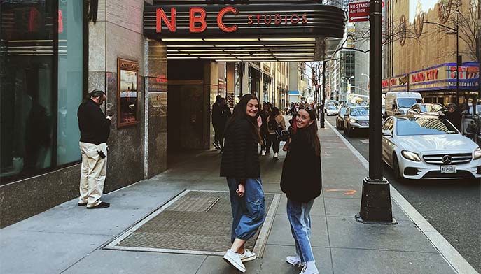 Image of two women posing together in front of an NBC building, smiling and enjoying their time in the city.