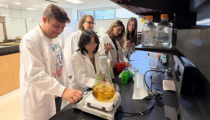 A group of students in lab coats collaborating on a science project at a lab table.