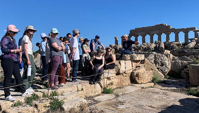 Image of a group of people gathered on the steps of an ancient building, enjoying the historic architecture around them.