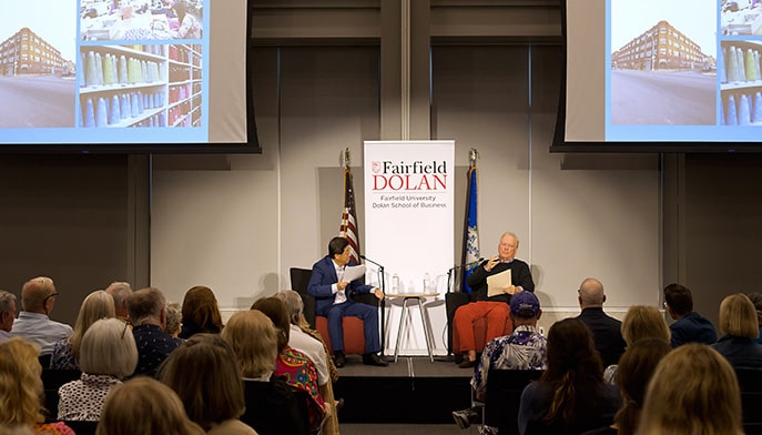 Fairfield Dolan dean speaking on a stage with Jay McLaughlin '70 during a Dean's Executive Forum lecture.