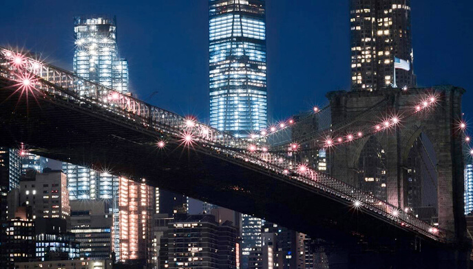 A nighttime view of the Brooklyn Bridge, illuminated against a dark sky, showcasing its iconic architecture and cables.