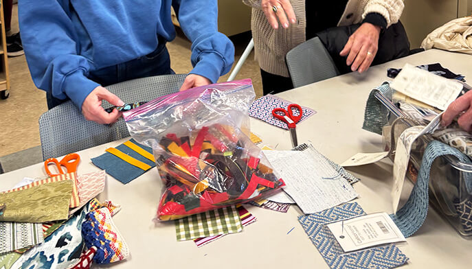 Students use scissors to cut a piece of fabric on a cutting mat, surrounded by sewing tools and materials.