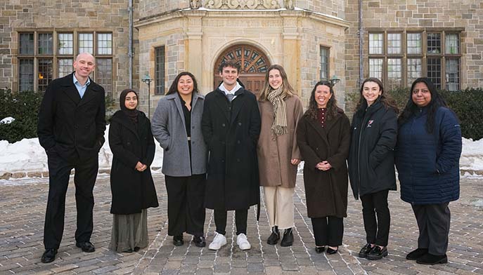 A diverse group of people posing in front of a building, looking happy and engaged.