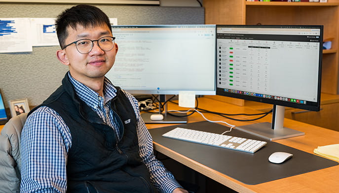 Fairfield Dolan professor sitting at his office desk with two monitors worth of analytical data.