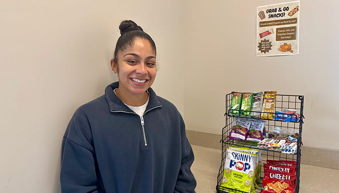 Public health senior posing with her healthy snack program organizational shelf.