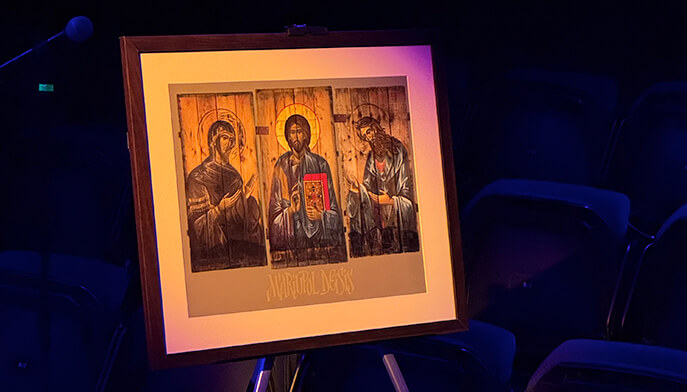 A framed photograph features three figures, each with halos, centered in soft light against a dark background. A serene, spiritual ambiance.